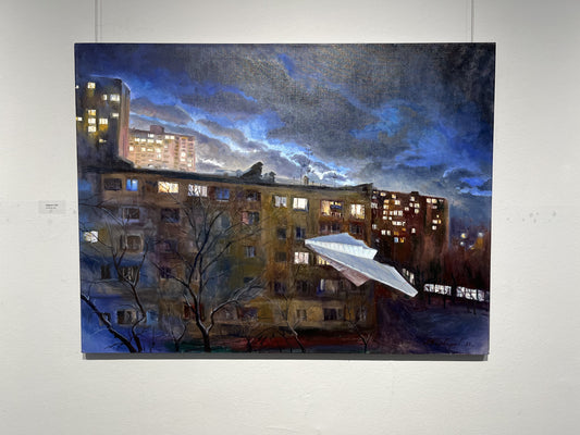 White paper airplane before lit apartments under dramatic night sky
