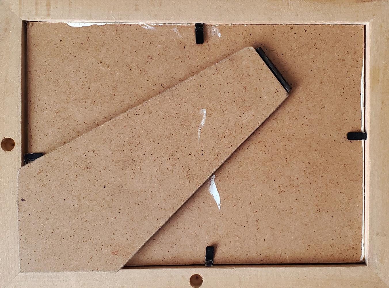 A light beige wooden picture frame with a visible particle board backing and black plastic corner brackets.