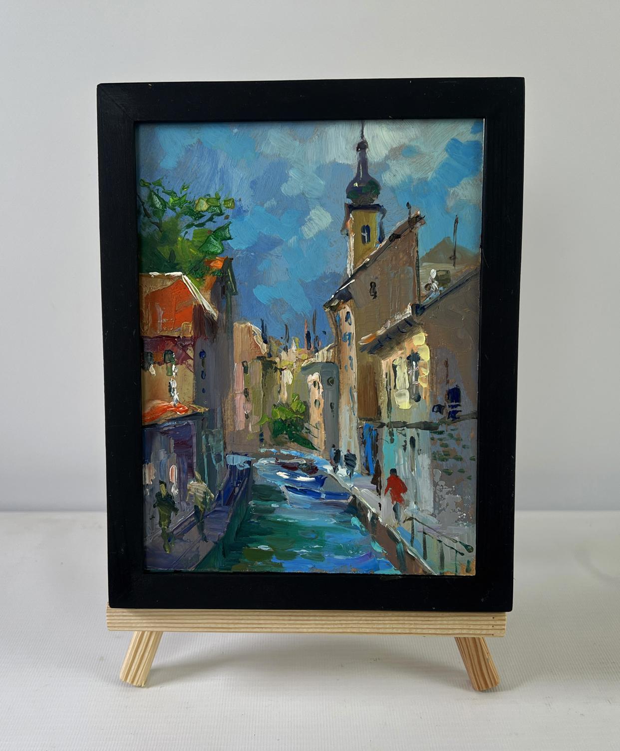 Black-framed oil painting of sunlit canal by Yuriy Suprunchuk on easel