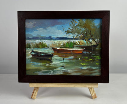 Oil painting of boats moored on shore by Yuriy Suprunchuk in dark frame