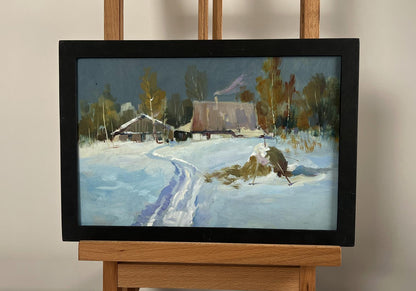 A framed winter landscape painting with snow-covered cottages and trees, enclosed in a simple black frame.
