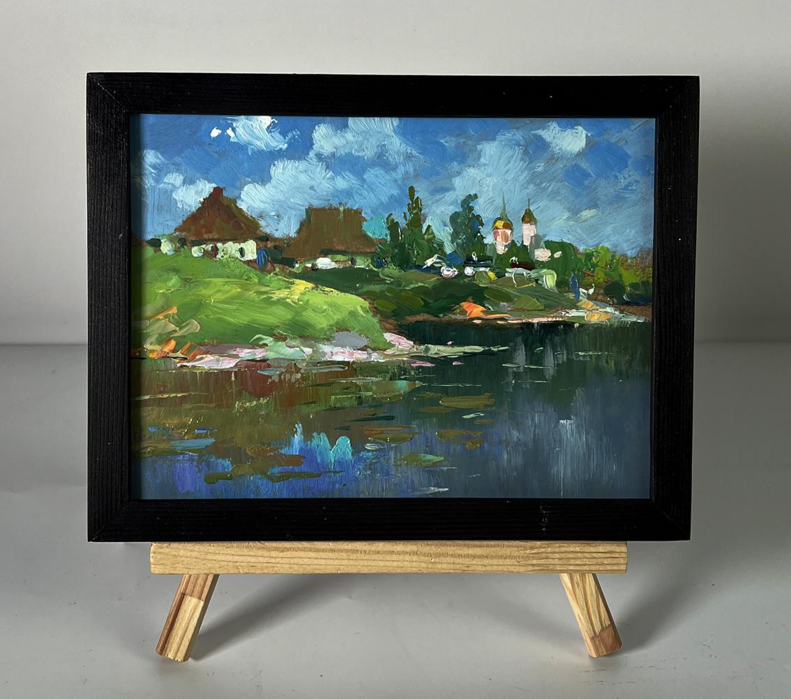 Oil painting of river near village by Yuriy Suprunchuk in black frame on easel