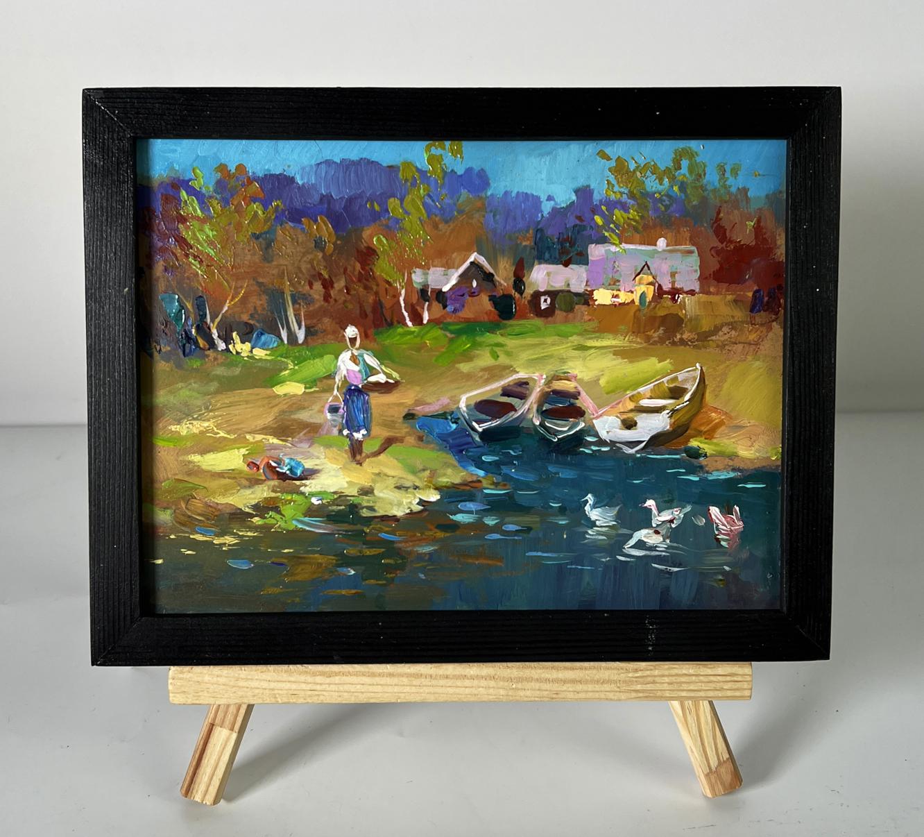 Black-framed oil painting by Yuriy Suprunchuk of geese swimming near river village with boats