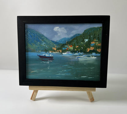 Black-framed oil painting by Yuriy Suprunchuk of lakeside village with boats