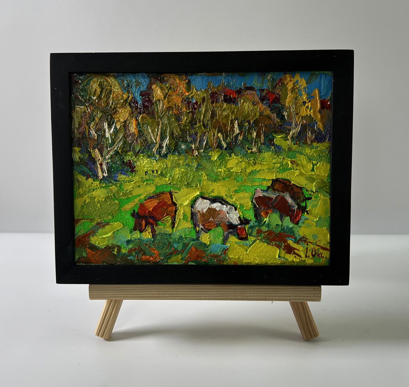 Vibrant oil painting of cows grazing in meadow by Oksana Ivanyuk on wooden easel