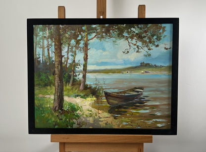 A framed oil painting depicting a serene lakeside scene with trees, grassy banks, and a small wooden rowboat resting in shallow water.