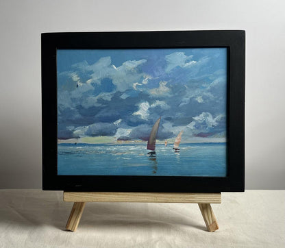 Black-framed oil painting of sailboats on blue sea under dramatic clouds by Yuriy Suprunchuk