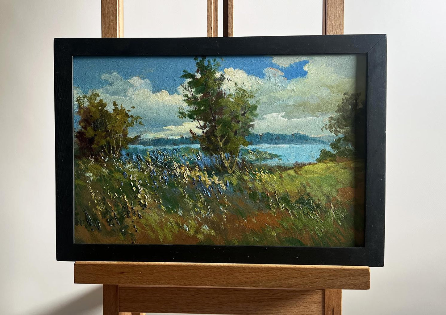 Oil painting by Yuriy Suprunchuk: flower field, river, lush trees, serene water