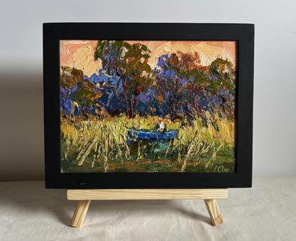 Oil painting of blue boat among golden reeds by Oksana Ivanyuk in black frame