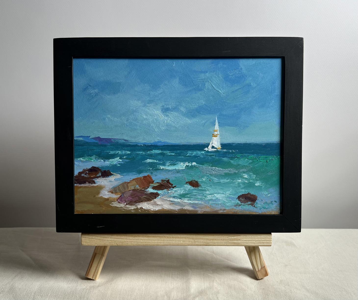 A framed oil painting depicting a sailboat on turbulent blue-green waters with rocky shores, enclosed in a sleek black frame.