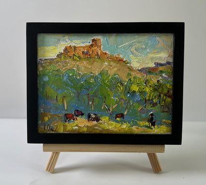 Oil painting by Oksana Ivanyuk: rustic hillside with grazing animals, old house in black frame