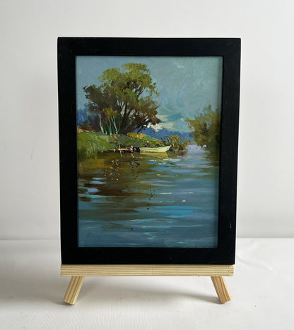 Black-framed oil painting of serene river boat ride by Yuriy Suprunchuk on easel