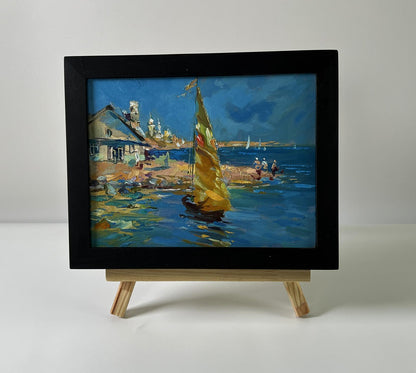 Framed oil painting of house on seashore with yellow sailboat by Yuriy Suprunchuk