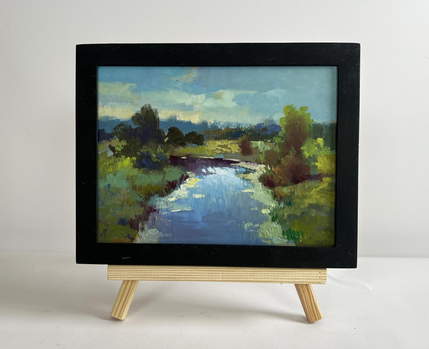 Black-framed oil painting of sunset clouds over serene river by Yuriy Suprunchuk
