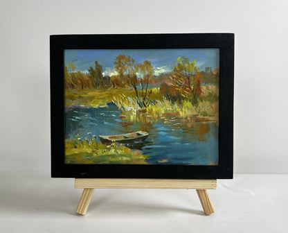 Black-framed impressionistic oil painting of autumn river with boat by Yuriy Suprunchuk