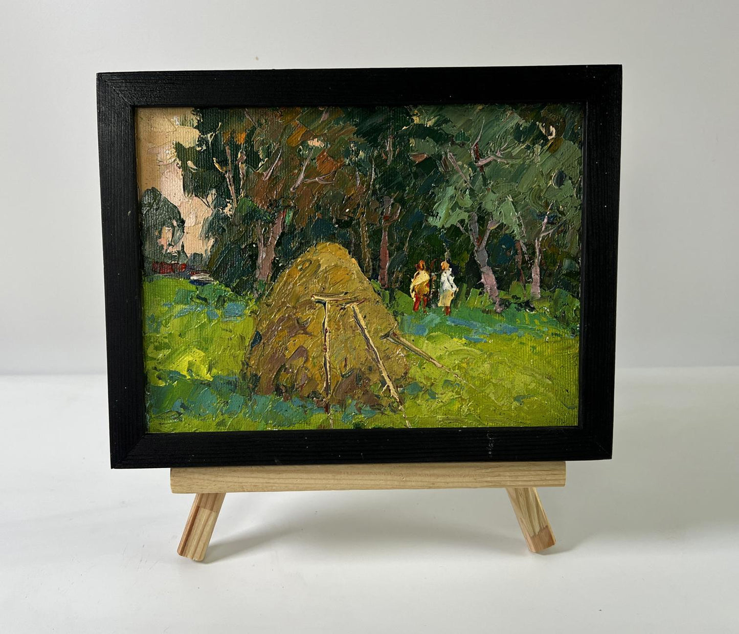 Oil painting of haystack near forest by Oksana Ivanyuk in black frame on easel