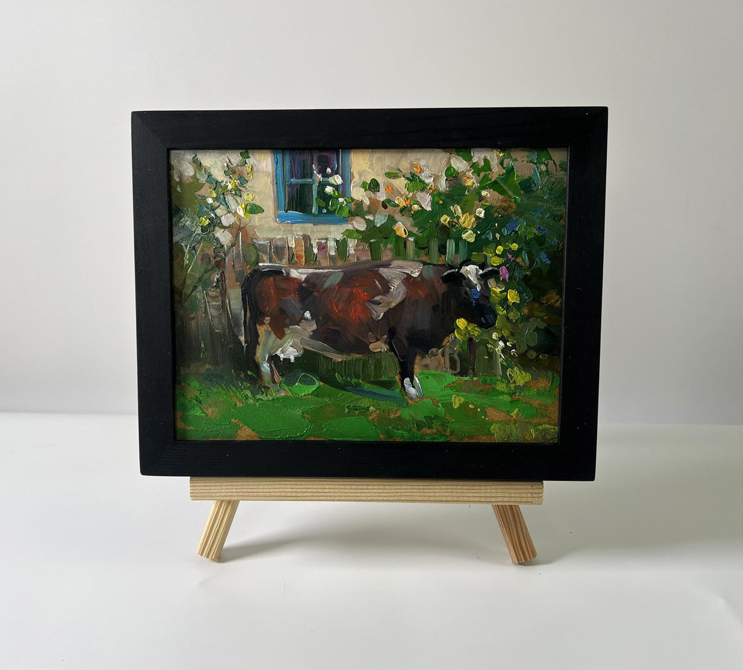 Black-framed oil painting of brown white cow in garden by Yuriy Suprunchuk