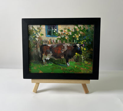 Black-framed oil painting of brown white cow in garden by Yuriy Suprunchuk