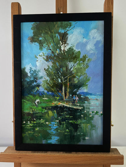 Black-framed oil painting of lush green tree by river bridge with people by Yuriy Suprunchuk