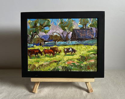 Vibrant impressionist oil painting of cows grazing on green field by Oleksiy Ivanyuk, framed on easel