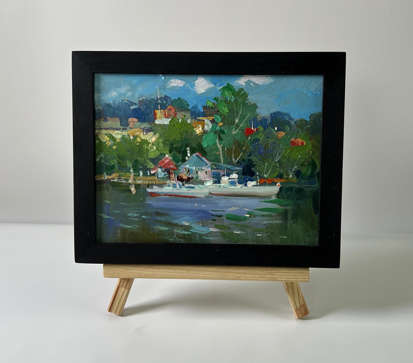 Black-framed oil painting of Yuriy Suprunchuk lakeside village with boats