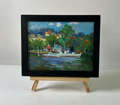 Black-framed oil painting of Yuriy Suprunchuk lakeside village with boats