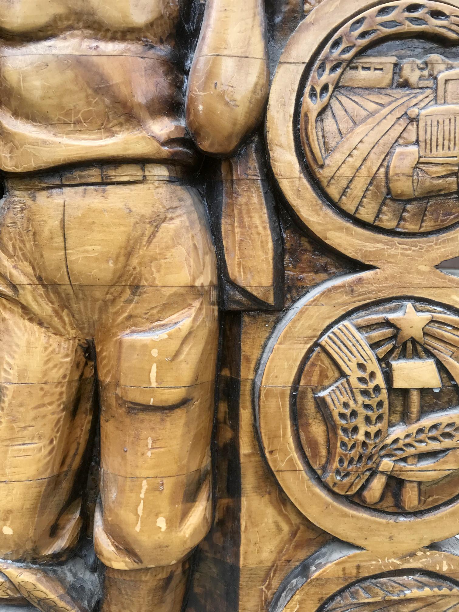 Carved wooden relief of muscular laborer in pants with agricultural industrial emblems, Social realism Communist Labor Brigade