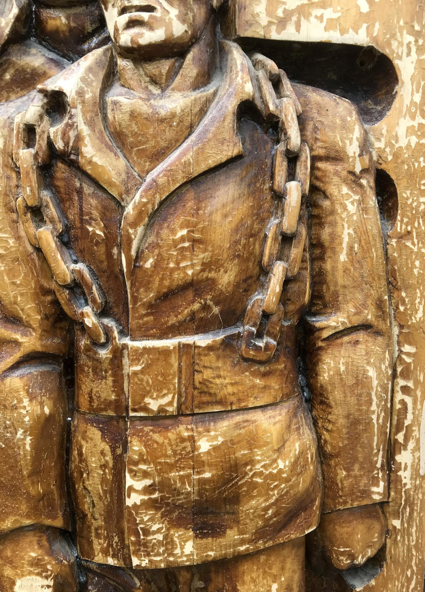 Detailed wooden carving of chained uniformed man in social realism style