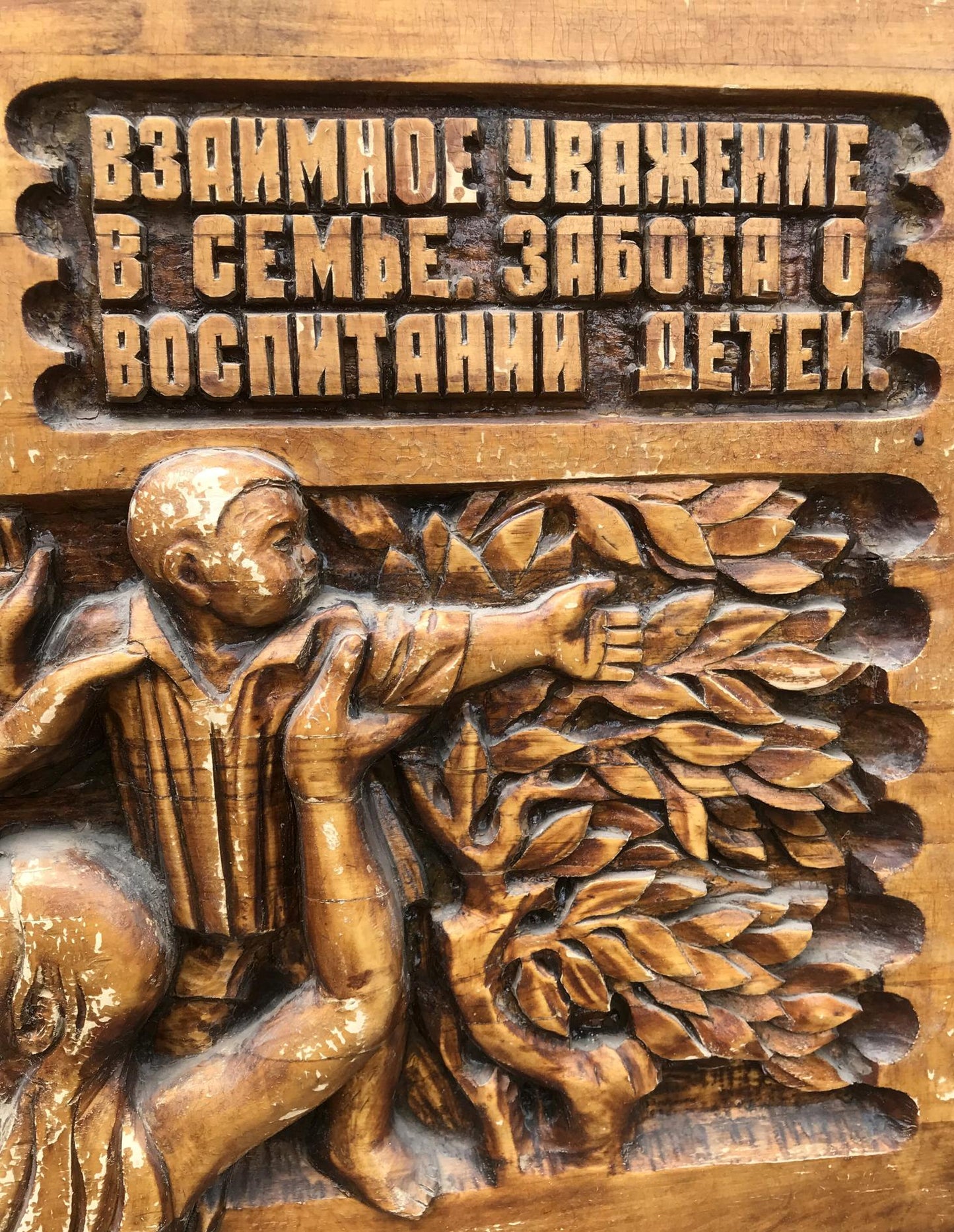Detailed wooden carving of boy reaching for leaves with R. text, Social realism family respect