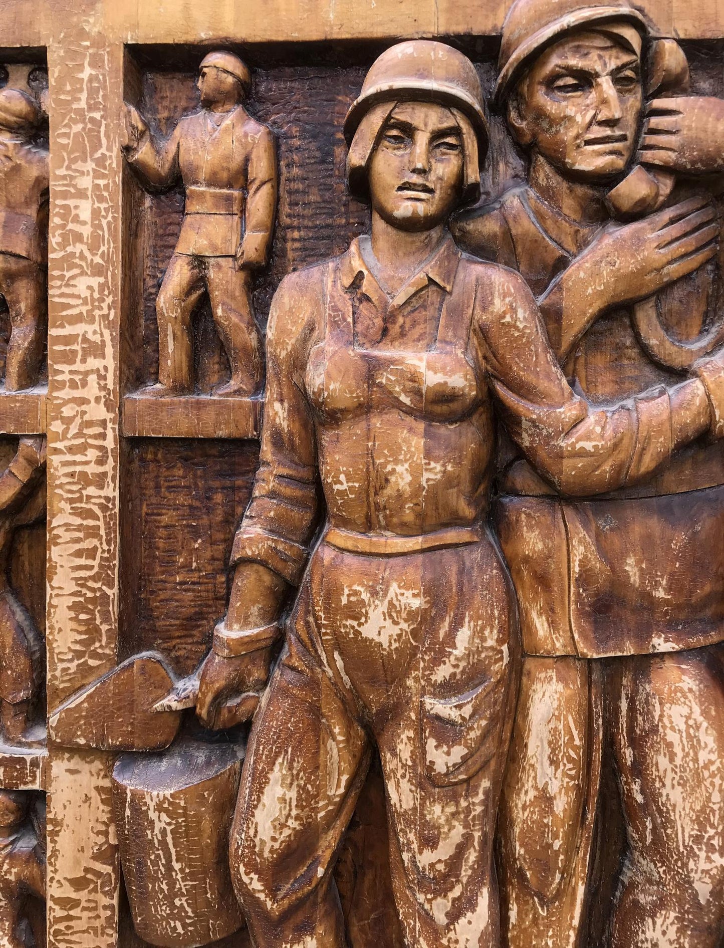 Bronze wooden relief of woman in military uniform beside figure, social realism art