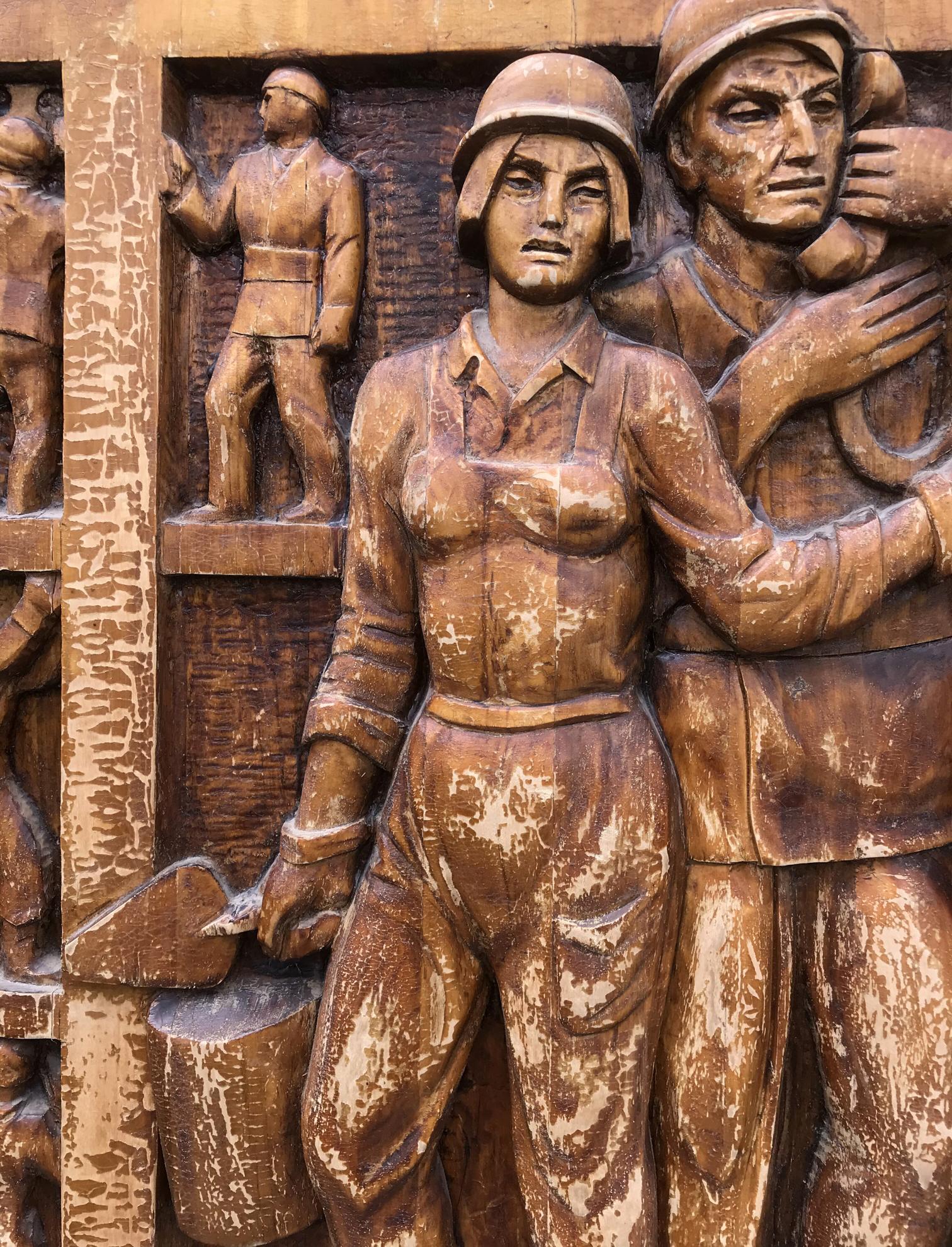Bronze wooden relief of woman in military uniform beside figure, social realism art