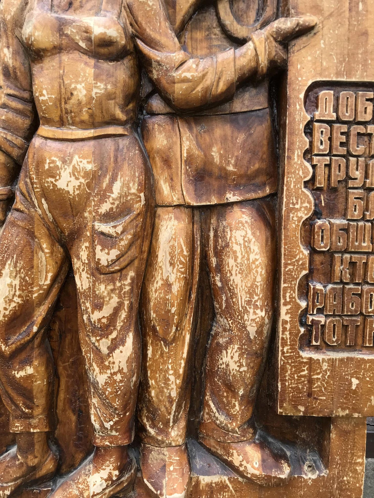 Weathered brown wooden relief of two workers in social realism sculpture