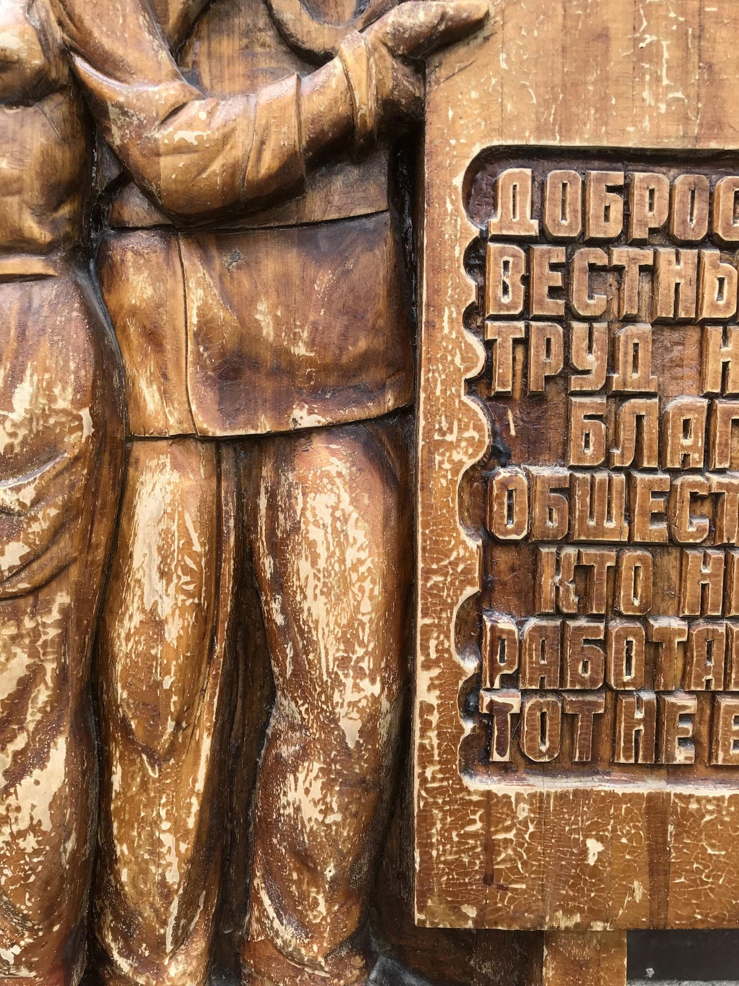 Weathered wooden relief of uniformed figure by Cyrillic plaque, social realism art