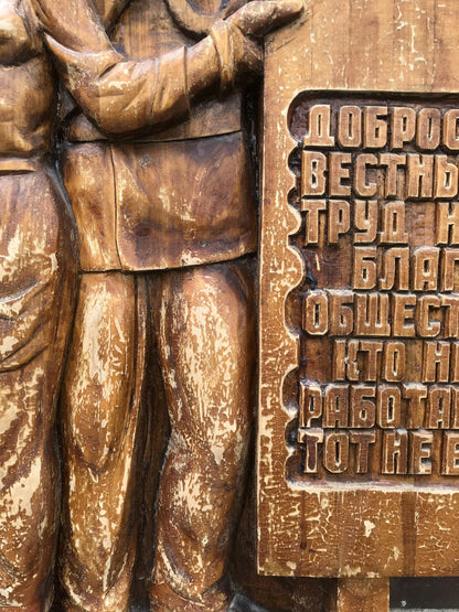 Weathered wooden relief of uniformed figure by Cyrillic plaque, social realism art