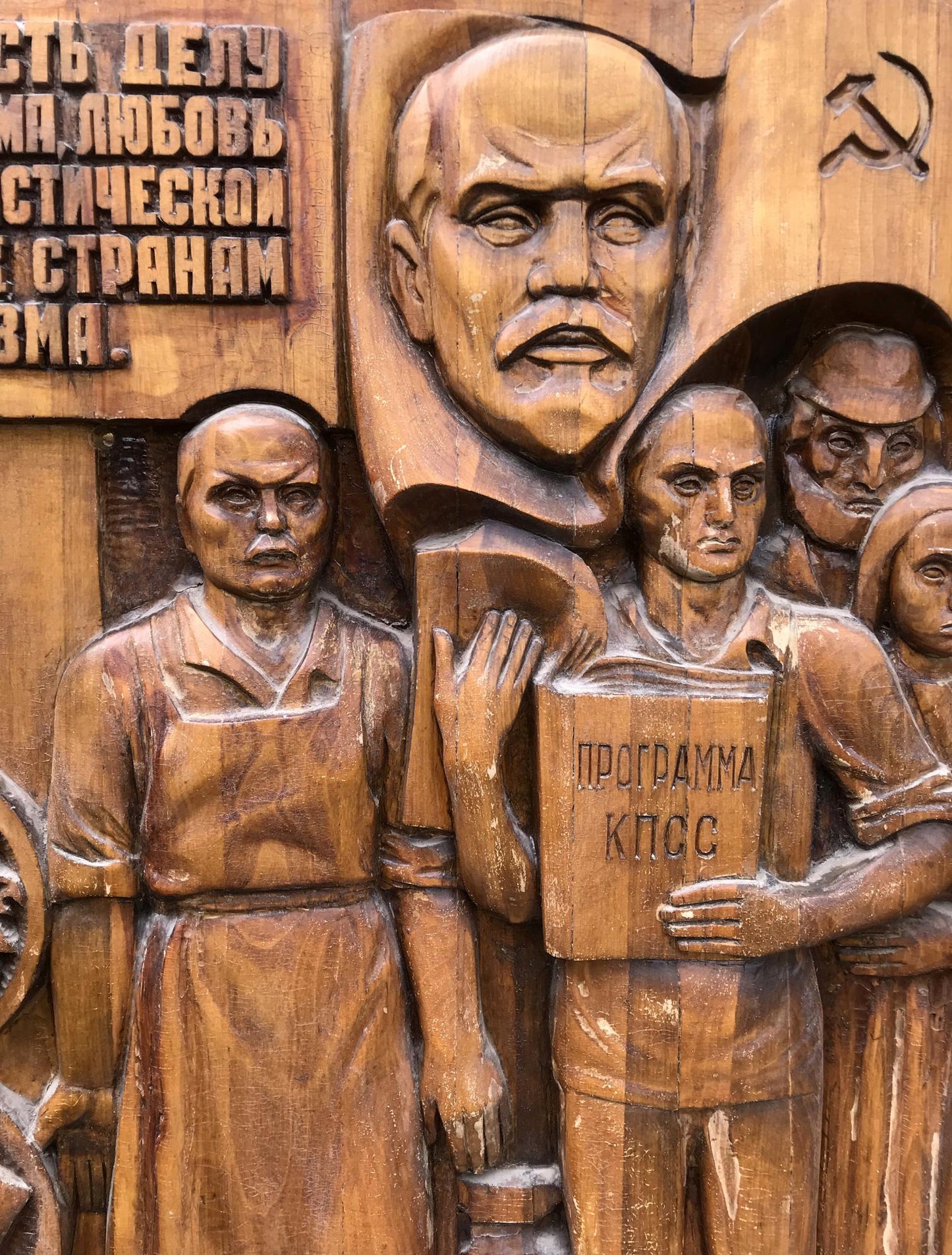 Wooden relief of mustached figure holding КПСС program in social realism style