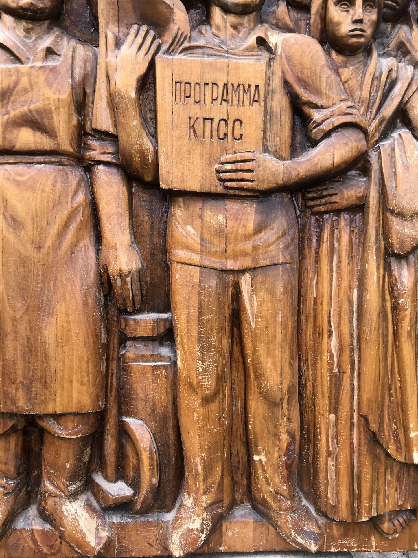 Wooden relief of social realism figure holding book with Cyrillic text