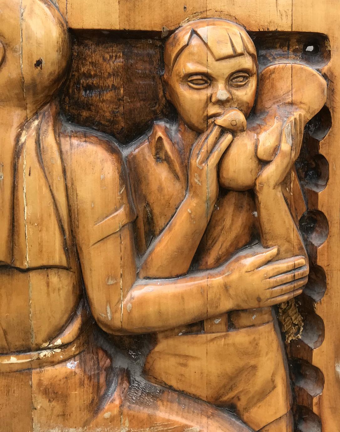 Intricately carved wooden relief of breastfeeding figure in social realism fraternal solidarity style
