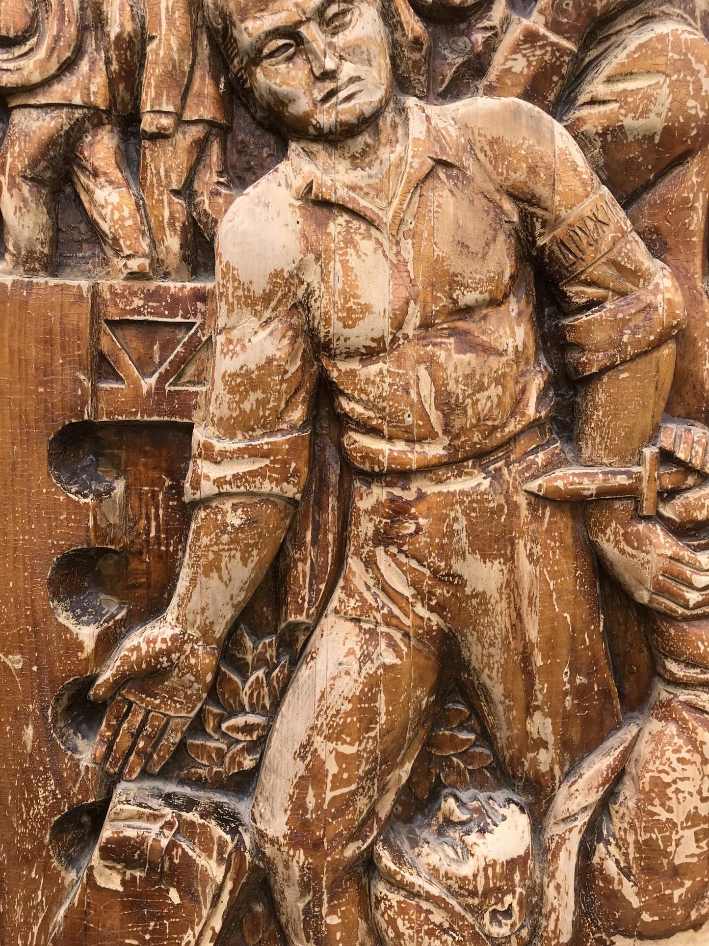 Weathered wooden relief of muscular man in historical attire holding dagger, embodying social realism public duty