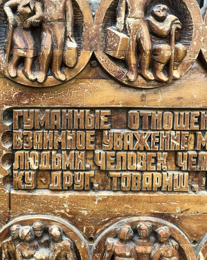 Bronze-toned wooden panel with social realism relief figures and R. text