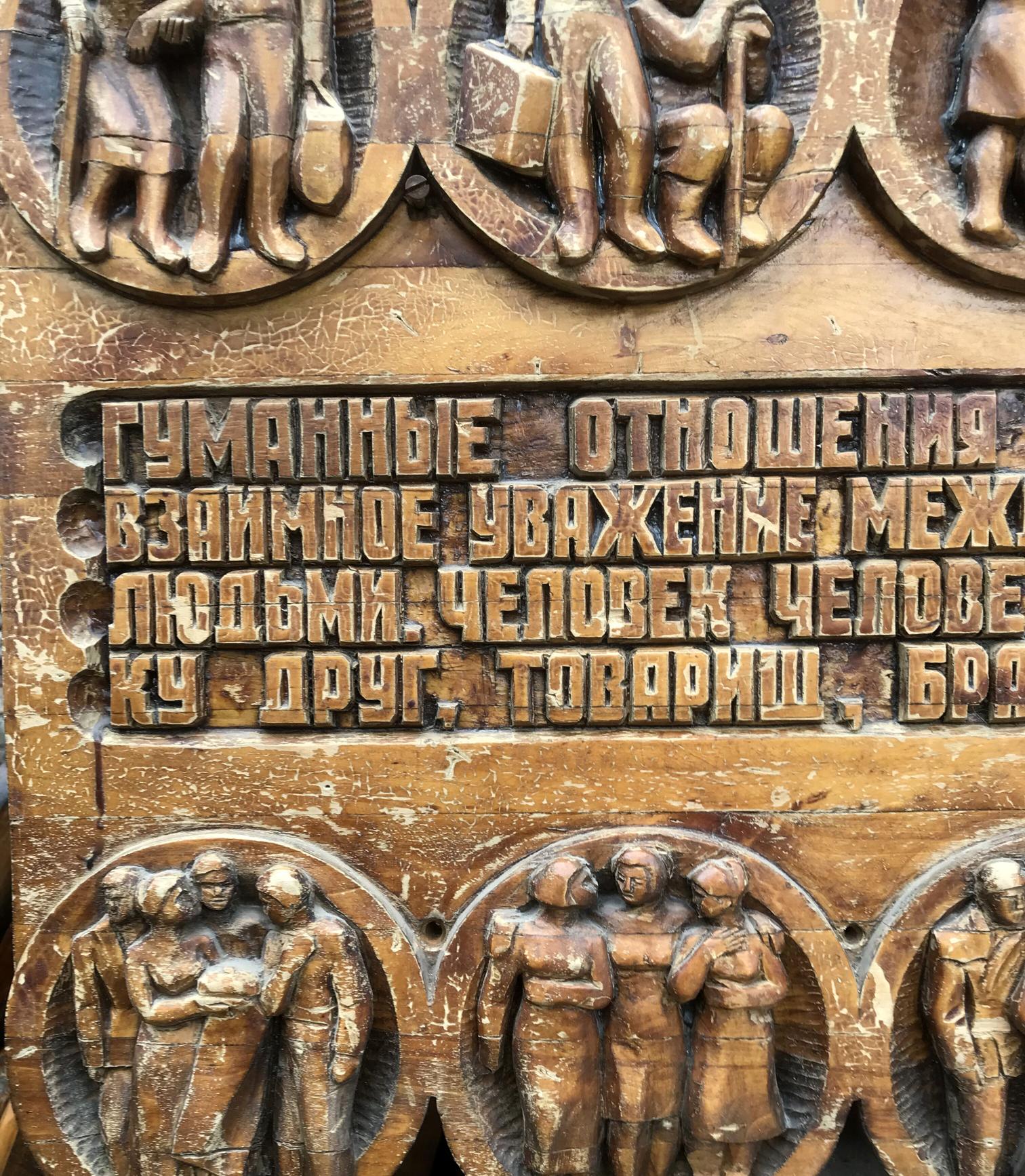 Carved wooden plaque with raised Cyrillic text and bronze-like figure reliefs