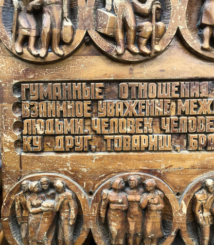 Carved wooden plaque with raised Cyrillic text and bronze-like figure reliefs