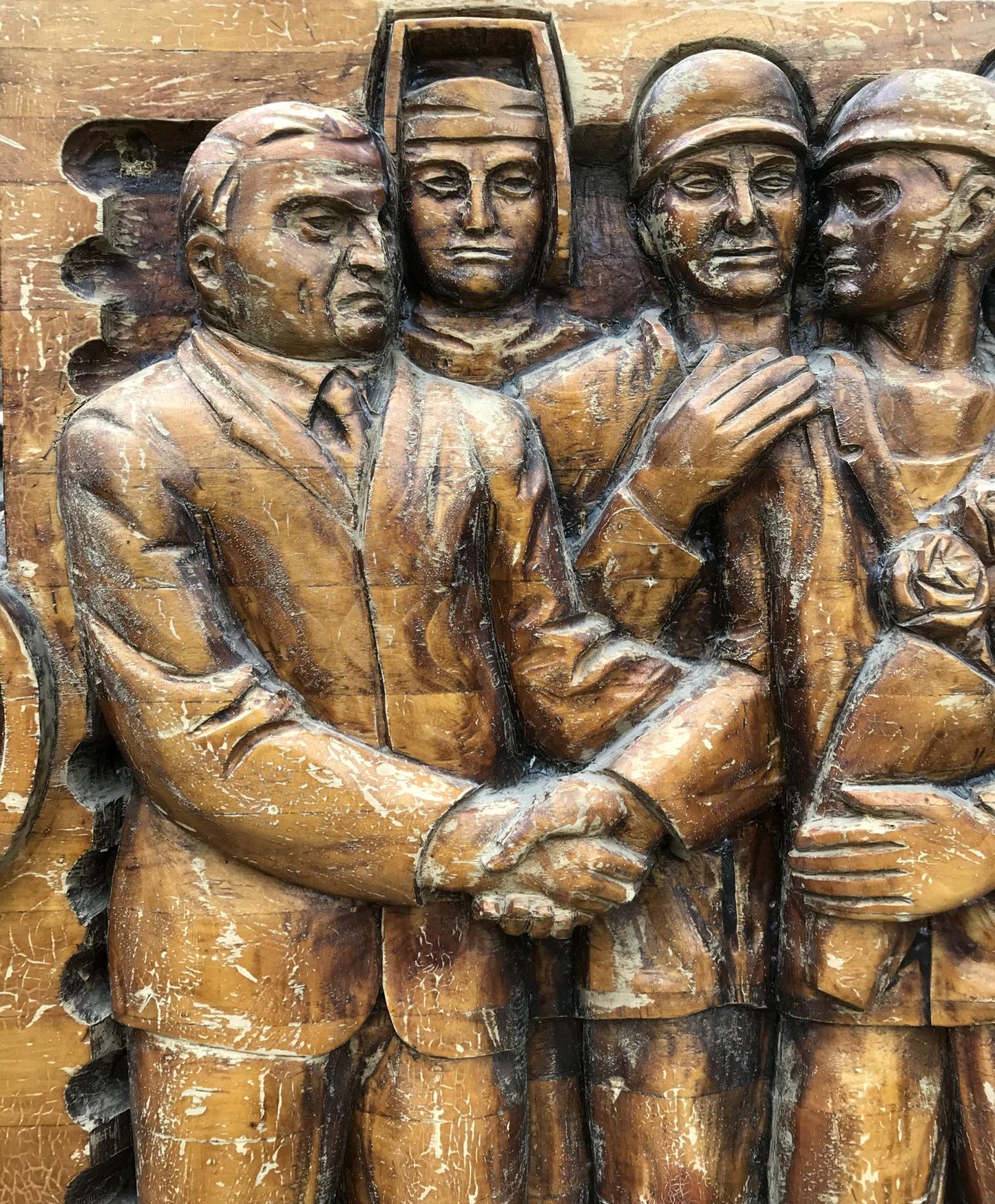 Carved wooden relief of social realism: four figures in formal attire, helmeted central figure, rose holder