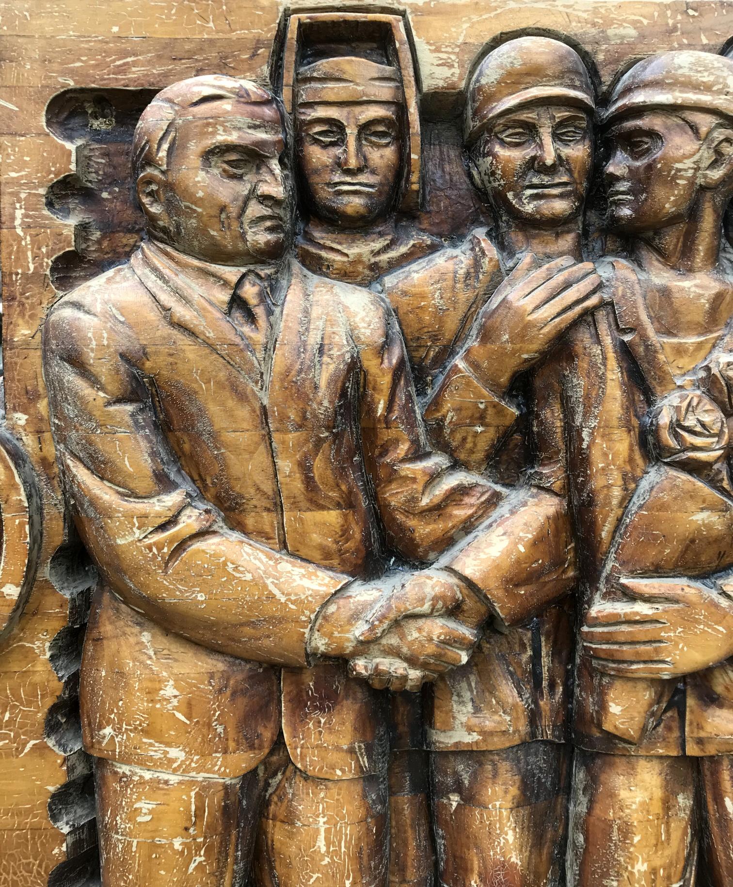 Carved wooden relief of social realism: four figures in formal attire, helmeted central figure, rose holder