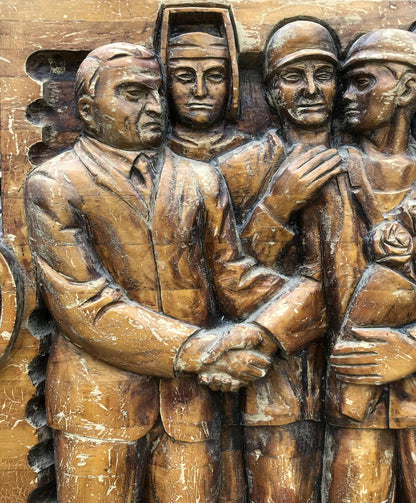Carved wooden relief of social realism: four figures in formal attire, helmeted central figure, rose holder