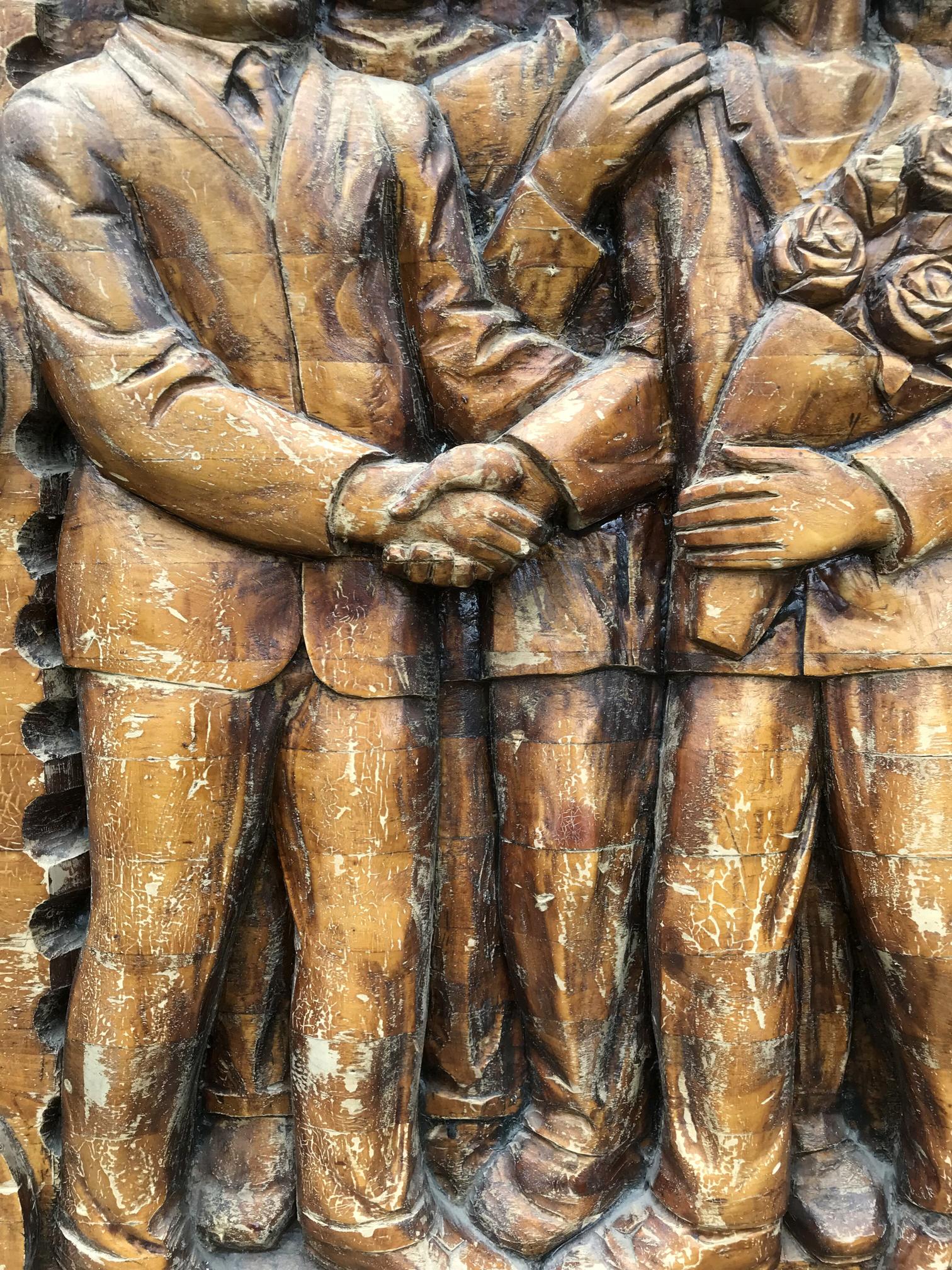 Bronze-toned wooden relief of suited men shaking hands in social realism style