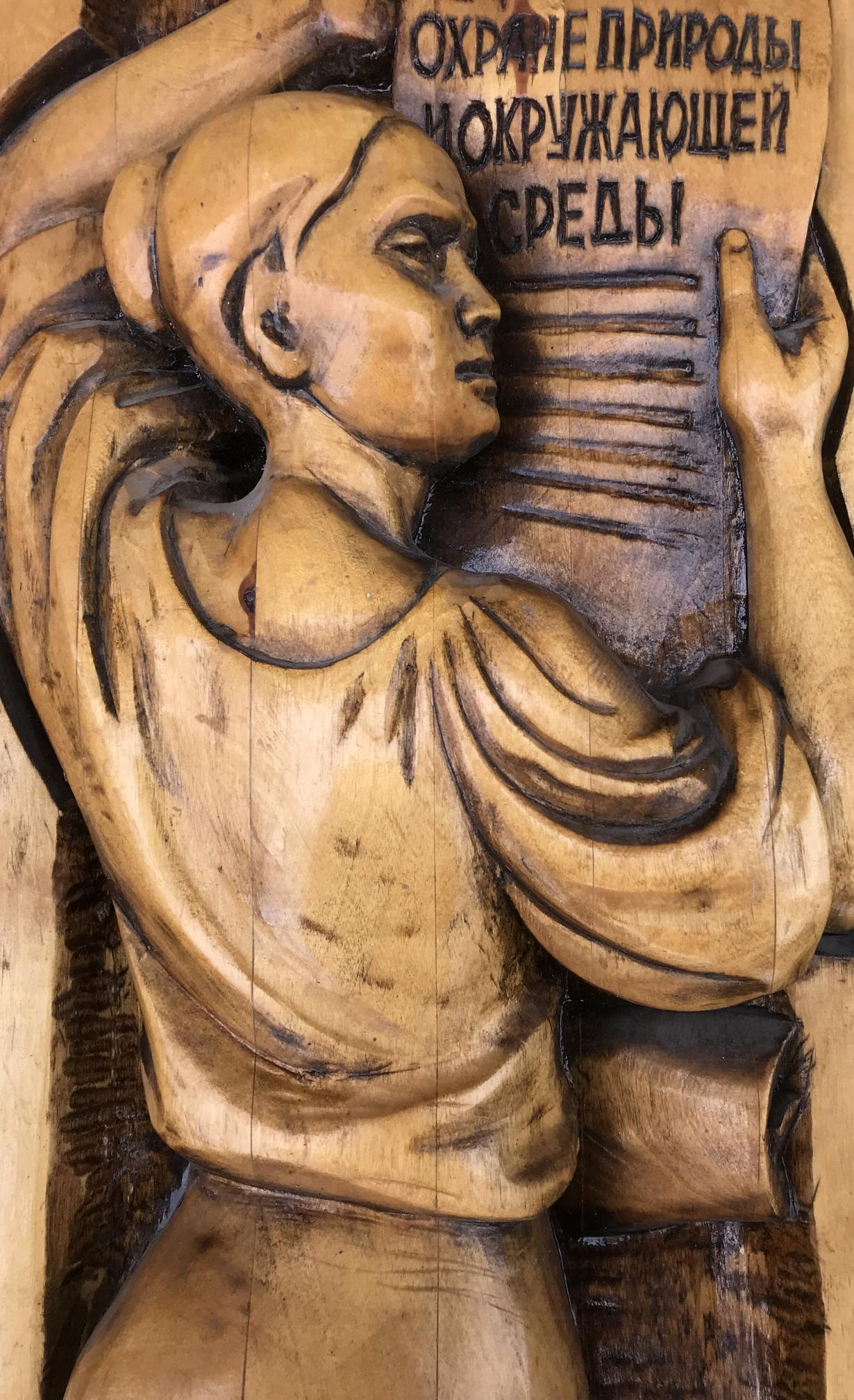 Detailed wooden carving of social realism figure holding scroll with R. text