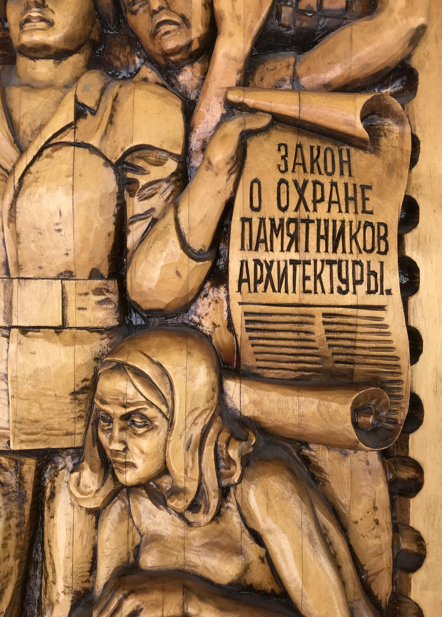 Detailed wooden relief carving of Social realism figures, scroll with R. text
