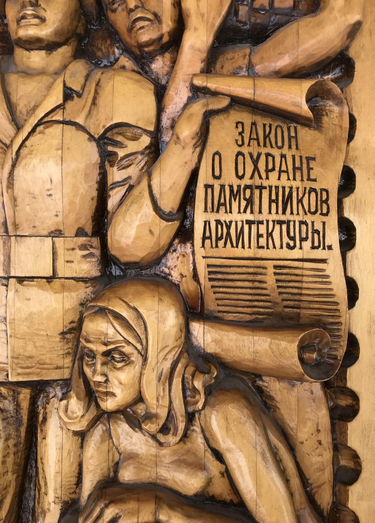 Detailed wooden relief carving of Social realism figures, scroll with R. text
