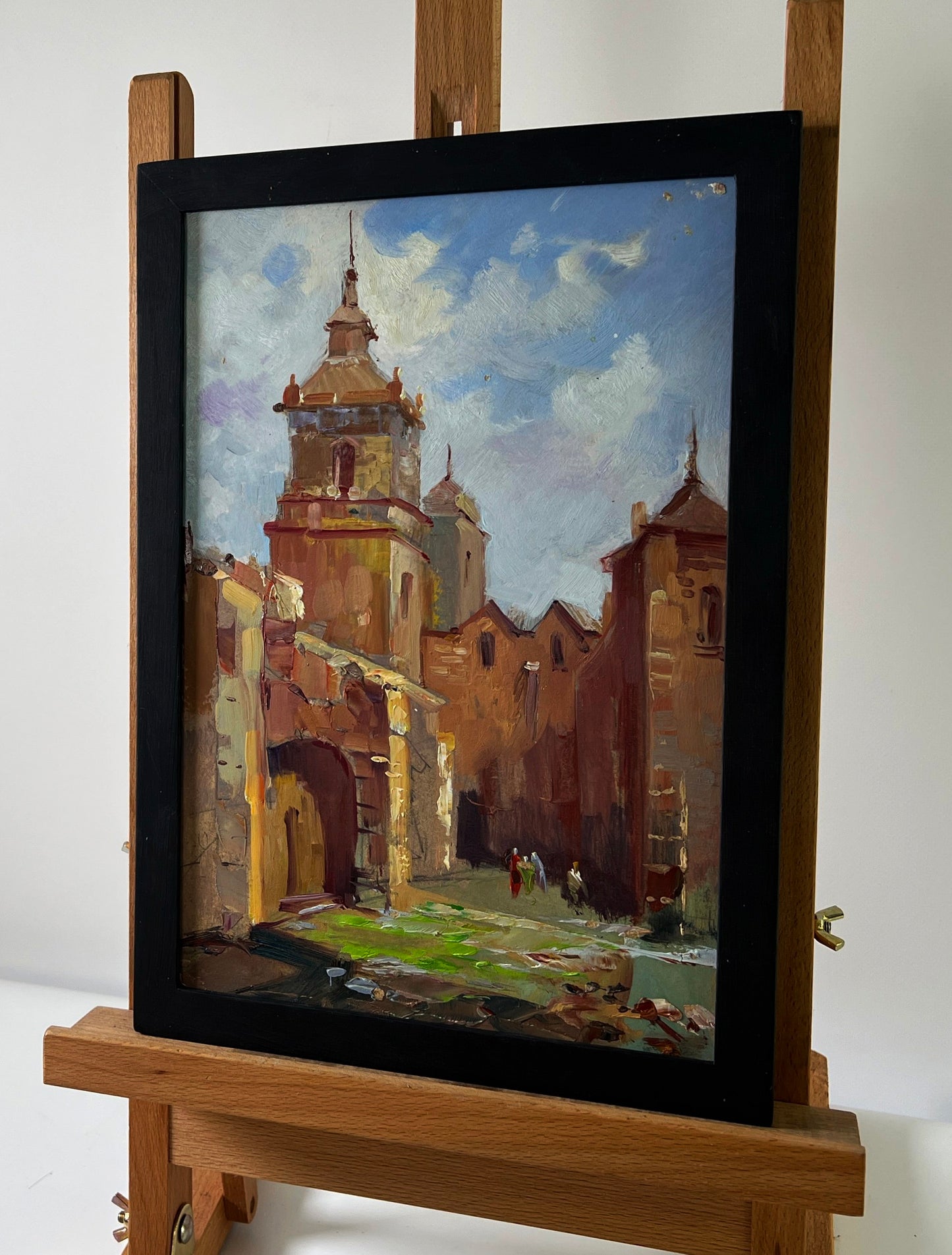 Framed oil painting of sunlit European street by Yuriy Suprunchuk on easel