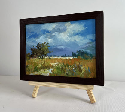 Framed oil painting of sun shining through clouds in pastoral landscape by Yuriy Suprunchuk